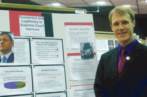 Photo of student standing with research presentation at URCAD campus event. 