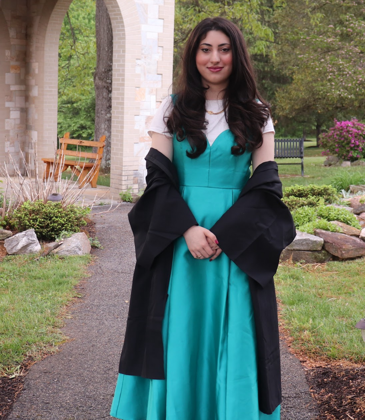 Hira Khan in an outdoor setting with flowers, wearing a teal dress with a black gown.